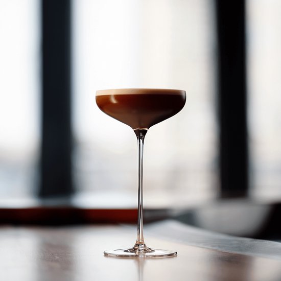 Kristallen champagneglas met een koffiekleurige cocktail, lange steel en brede kelk.