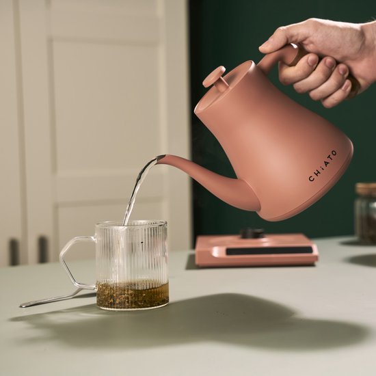 Roze waterkoker met slanke tuit, water wordt in een geribbelde mok gegoten.