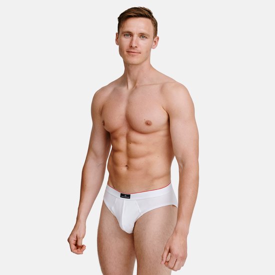 Man met witte slip met rode bies aan de tailleband, staand met lichte glimlach.