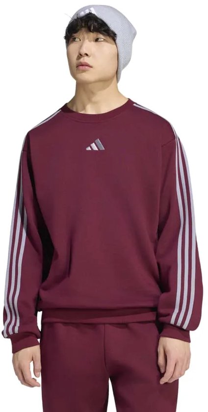 Man in bordeauxrode sweater met grijze strepen op de mouwen en een logo op de borst.