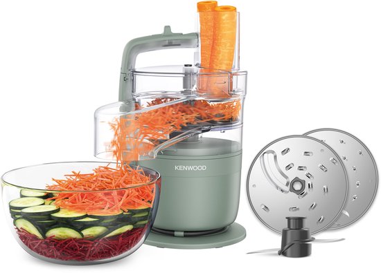 Groene Kenwood foodprocessor met geraspte wortelen en courgette in een glazen kom, naast snijschijven.