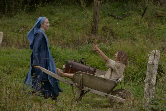 Meisje in kruiwagen duwt lachwekkend achteruit, terwijl een vrouw in blauw habijt trekt.