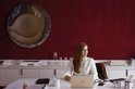 Vrouw met rood haar in witte blouse zit aan bureau met laptop.