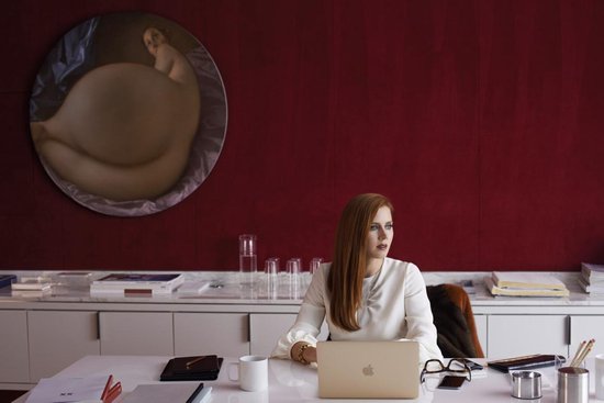 Vrouw met rood haar in witte blouse zit aan bureau met laptop.