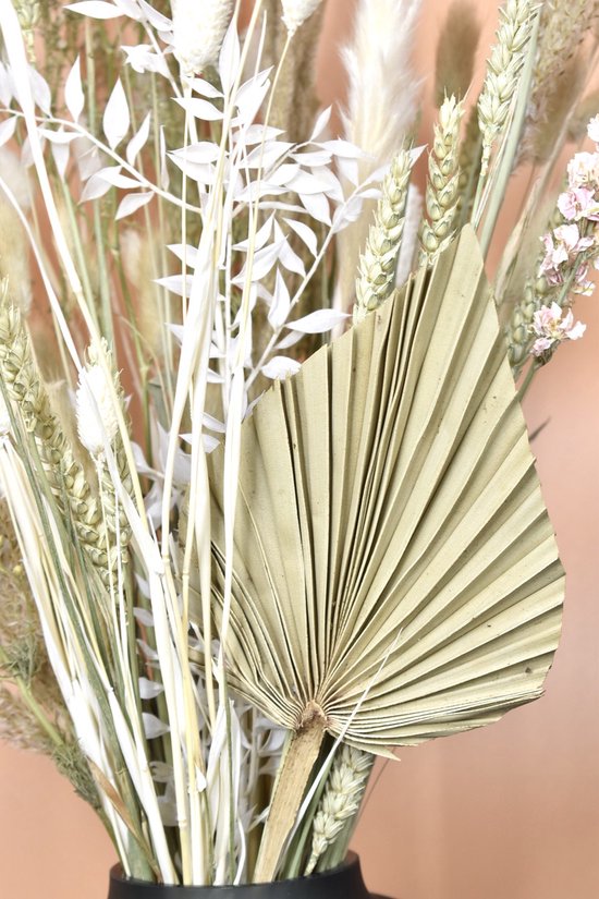 Gros plan d'un éventail de palmier séché au centre d'un bouquet de fleurs séchées, avec des épis de blé et des panaches.