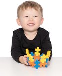 Een lachende jongen met een zwart shirt houdt een ronde, gele en oranje Plus-Plus constructie vast.