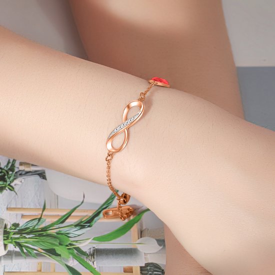 Rosegouden armband met oneindigheidssymbool en een rood hartje, gedragen om een arm.