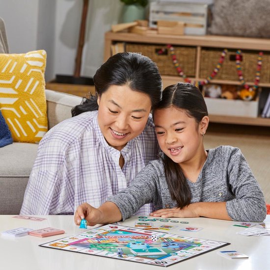 Een vrouw en een meisje spelen Monopoly Junior aan een tafel.