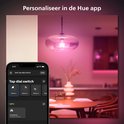 Een telefoon toont de Hue app met de Tap Dial Switch instellingen, met een woonkamer met roze verlichting op de achtergrond.