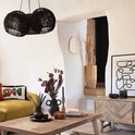 Gouden spiegel in organische vorm, hangend in een woonkamer met een gele bank en zwarte lampen.