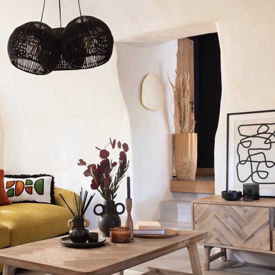 Gouden spiegel in organische vorm, hangend in een woonkamer met een gele bank en zwarte lampen.