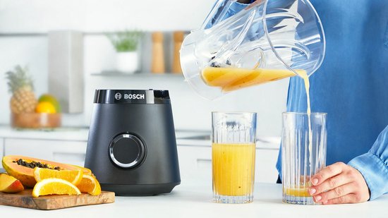 Zwarte Bosch blender in een keukenomgeving, waarbij sap uit de kan in twee glazen wordt geschonken.
