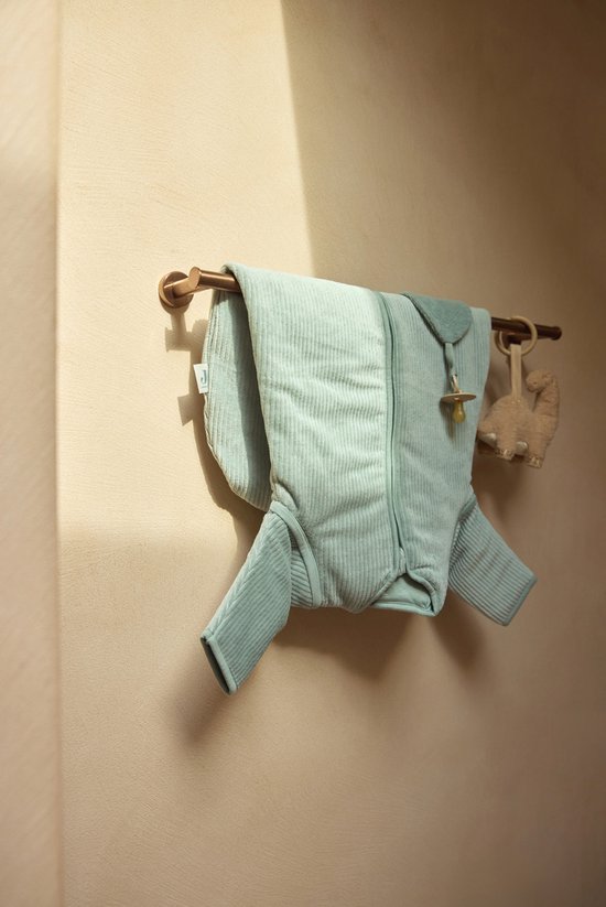 Lichtgroene baby slaapzak met ribbelstructuur, hangend aan een staaf met een fopspeen en knuffel dinosaurussen.