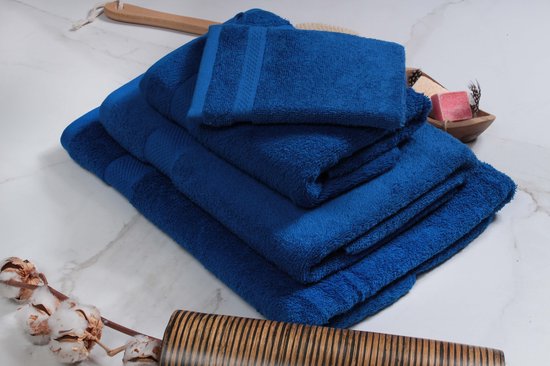 Une pile de serviettes bleu vif, y compris un gant de toilette, avec une brosse de lavage en bois et des branches de coton décoratives.