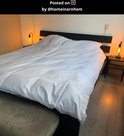 Twee moderne zwarte tafellampen met gloeilampen op nachtkastjes naast een groot bed met wit dekbed.