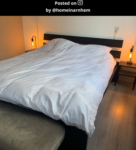 Twee moderne zwarte tafellampen met gloeilampen op nachtkastjes naast een groot bed met wit dekbed.