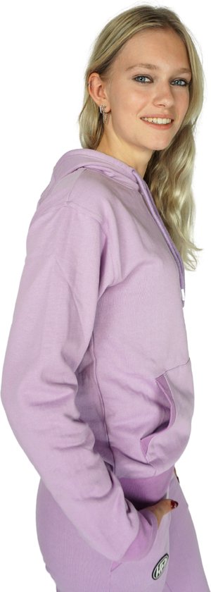 Model in een zachtpaars joggingpak met capuchon. Zijaanzicht met kangoeroezak en logo op de broek.