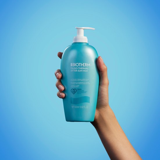 Een hand houdt een turquoise Biotherm "Oligo-Thermal After-Sun Milk" fles vast.