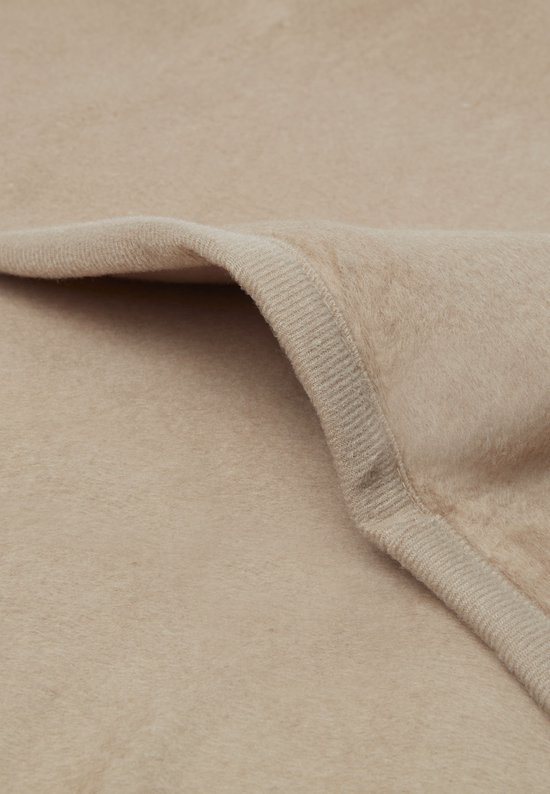 Detail van de zachte stof en de gebreide rand van een biscuitkleurige babydeken.
