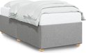 Structure de lit rembourrée gris clair avec matelas et draps blancs, sur pieds en bois.