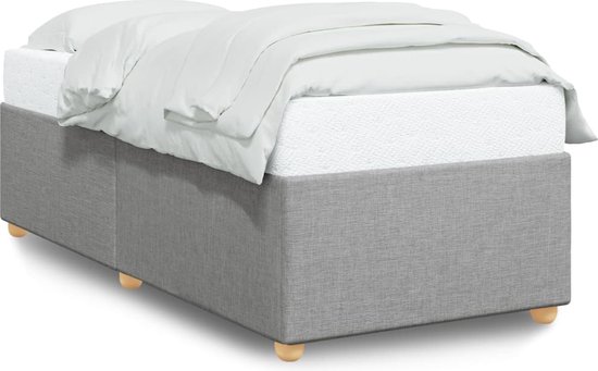 Structure de lit rembourrée gris clair avec matelas et draps blancs, sur pieds en bois.