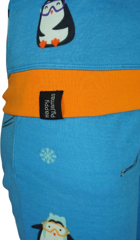 Detail van een blauwe pyjamabroek met oranje band en een 'Happy Pyjamas' label, versierd met pinguïns en sneeuwvlokjes.