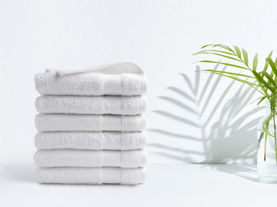 Stapel witte handdoeken op een witte achtergrond, met een plant op de achtergrond.