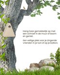 Lichtbeige driehoekig vogelhuisje hangt aan een boom met een vogel erop.