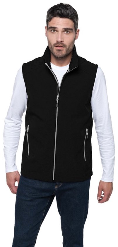 Man draagt een zwart mouwloos vest met rits en hoge kraag, wit shirt en spijkerbroek.