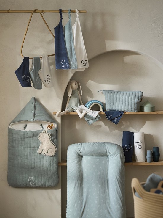 Opgehangen babytextiel, waaronder een lichtblauwe trappelzak met beer-applicatie, een konijn, regenbogen en toilettas.