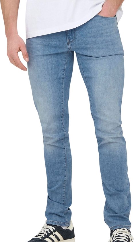 Man met hand in zak van lichtblauwe slim fit jeans, met sneakers.
