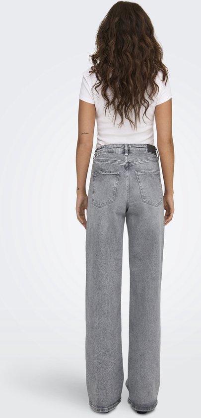 Model met lang golvend bruin haar, in een grijze jeans met wijde pijpen en een witte top.