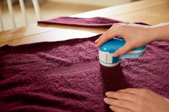 Hand gebruikt een lichtblauwe Philips pluizenverwijderaar op een paars wollen kledingstuk.