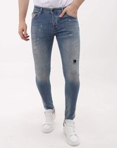 Man in een blauwe skinny spijkerbroek met scheuren en gaten, met witte sneakers.