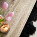 Close-up van het licht houten tafelblad met een grof patroon. Roze tulp in een vaas en een glazen windlicht met kaars.