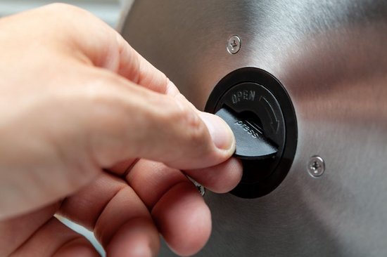 Hand draait een zwarte knop met 'open' en 'press' aanduiding op een metalen snijmachine.