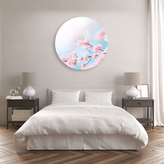 Cercle mural rond avec des branches de fleurs roses, au-dessus d'un lit blanc dans une chambre.