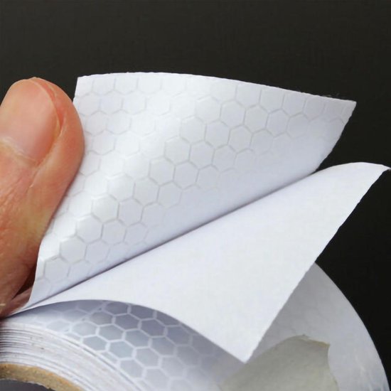 Een vingerafdruk verwijdert de achterkant van witte reflecterende tape met een honingraatpatroon.