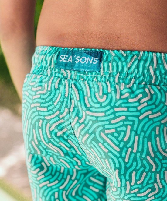 Close-up van de achterkant van een turquoise zwembroek met wit patroon en merklabel 'SEA'SONS'.