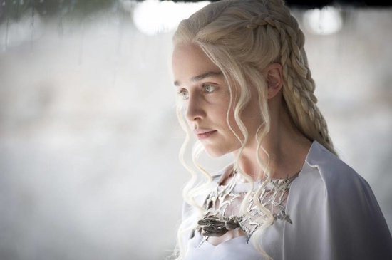 Close-up van een vrouw met gevlochten blond haar en een witte cape, met een zilveren ketting.