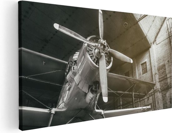 Photo noir et blanc d'un avion à hélice dans un hangar, avec l'avant de l'avion au centre.