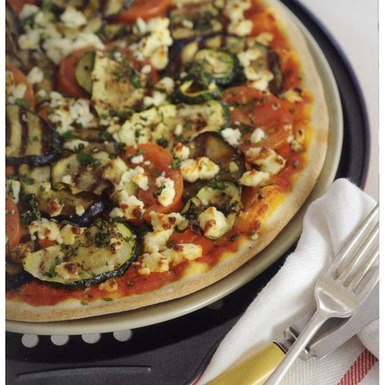 Pizza met aubergine, courgette, tomaat en feta, op een bord.