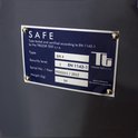 Blauw metalen plaat met witte tekst: SAFE, Type tested and certified according to EN 11443-1 by the TREZOR TEST s.r.o. Type EM 4, Security level 1, Serial No. / Year P000001 / 2012, Weight (kg) 94. TREZOR TEST s.r.o. Akkrediterte Sertifizierungsstelle.