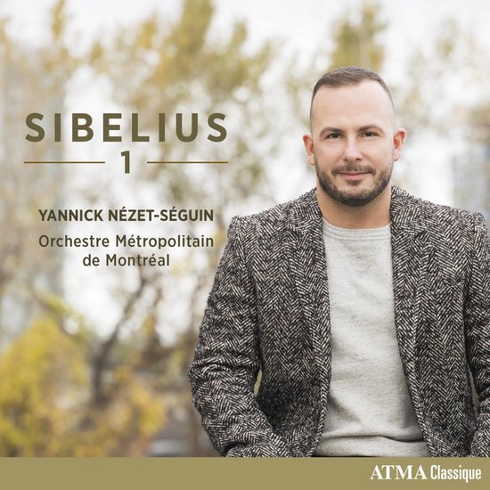 Man met kort donker haar en baard, gekleed in een grijs vest en een grijs-bruin geruit jasje, poseert met de handen in de zakken. Titel: SIBELIUS 1, YANNICK NÉZET-SÉGUIN, Orchestre Métropolitain de Montréal.