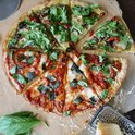 Pizza met pesto, rucola, zongedroogde tomaten en mozzarella, gesneden.