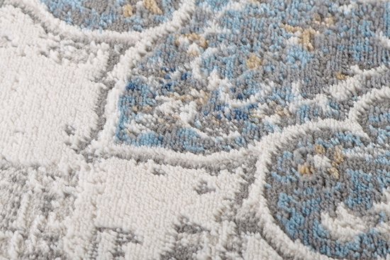 Gros plan d'un tapis rond gris montrant la texture usée et les fils bleus, blancs et gris du motif floral.