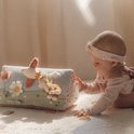 Baby speelt met een activiteitenboek in de vorm van een driehoek met bloemen, vogels en een vosje.
