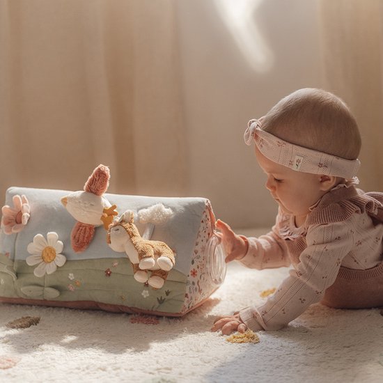 Baby speelt met een activiteitenboek in de vorm van een driehoek met bloemen, vogels en een vosje.