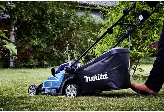 Turquoise Makita grasmaaier, gebruikt op gras met een grasvangzak en achtergrond van bomen.