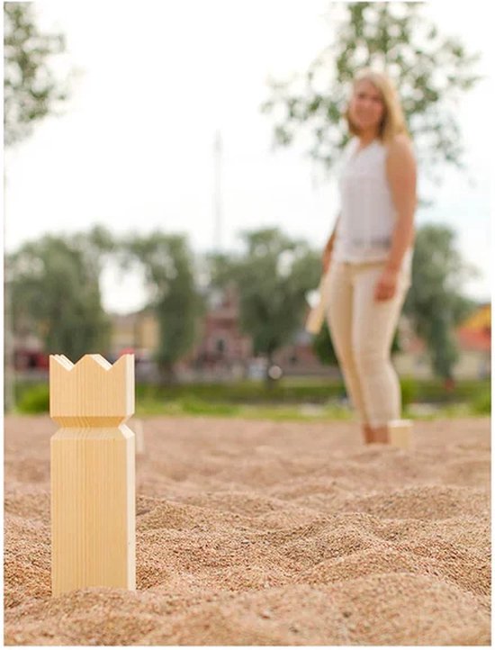 Houten koning skittle op zand, met een zacht gefocuste vrouw op de achtergrond.